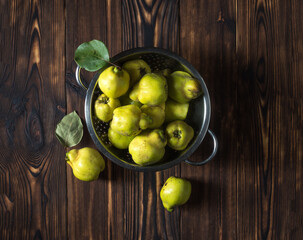 Large ripe quince fruits with leaves in a colander. View from above
