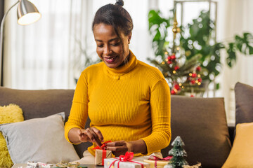 Getting Ready for Christmas: Young Smiling African-American Woman wrapping Christmas Presents for her Loved Ones at Home