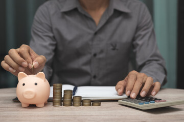saving money and accounting concept. business man putting coin insert to piggy bank and make...