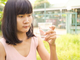 Asian woman holding glass with cold water for drink and blur green nature background. authentic skin tan, black hair and slim fit. drink water in morning. lifestyle food for good health concept.