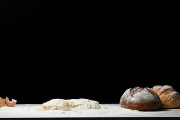 Cooking the bread. Freshly baked bread and prepared dough for baking on a black background. Space for text. The concept of nutrition.