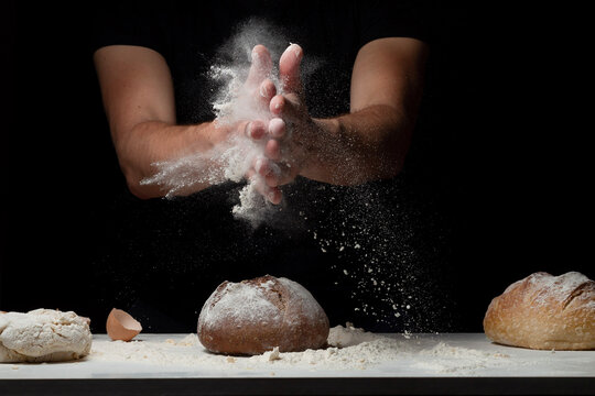 Cooking bread. Hands with flour splash and flying on white table covered with flour from his hands. Chef clap white flour dust man hand on black background. Space for text. The concept of nutrition