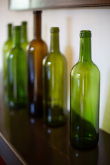 Empty green wine bottles are on a wooden shelf. 
Vertical image.