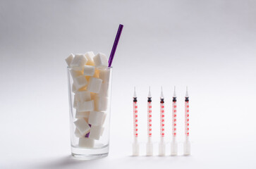 A full glass of sugar similar to a sweet cocktail and several syringes for diabetics on a neutral...