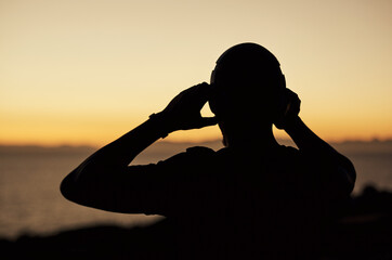 Silhouette shot of a young man listening to music while standing outdoors 