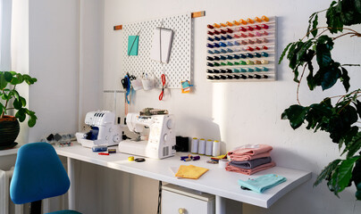 A tailor's workspace in a spacious white room. Large white table with sewing machine and overlock.