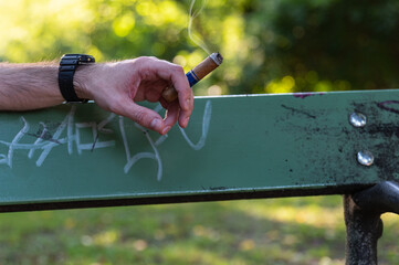 Mann auf einer Parkbank mit Zigarre in der Hand