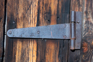An old metal rusty hinge on a door made of dark old wood. Close-up. Hard daylight.