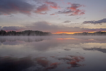 Foggy autumn landscape at dawn of the shoreline of Whitford Lake with mirrored reflections in calm water, Fort Custer State Park, Michigan, USA