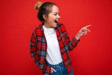 Portrait of beautiful fascinating emotional positive joyful happpy female promoter pointing to the side at copy space for advertising wearing hipster outfit isolated over background wall with empty