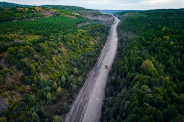 Fototapeta na wymiar Large yellow truck rides through forest to be loaded into open coal mine
