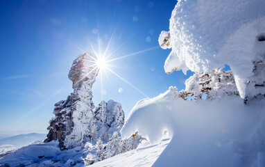 Clear winter day beauty landscape, frozen trees and rocks in the snow, blue sky with sunbeams