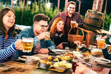 Happy men and women having fun drinking beer at patio garden fest - Social gathering life style concept on young friends enjoying hangout time together at night - Warm filter with focus on left guy