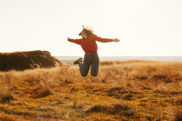 Full body portrait of a young woman jumping in a field on a sunny day.