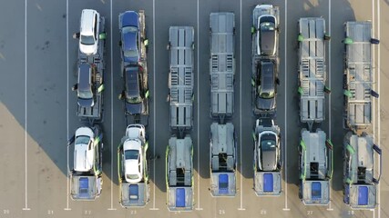 Aerial top down view of a car carrier trailers (car-carrying trailer, car hauler, or auto transport trailer) with a new cars on it stand on a parking lot of a dealership or customs terminal
