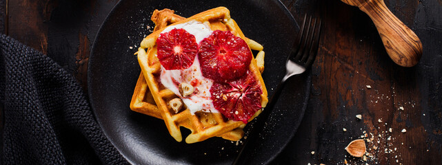 Waffles with yogurt and red Sicilian orange sauce on old dark wooden background. Top view