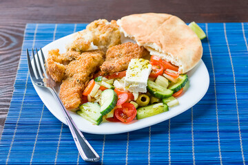 Baked fish served with vegetable salad with feta cheese