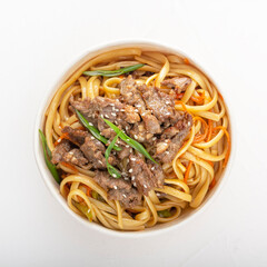 Noodles with meat, pepper and herbs in a paper disposable plate on a white background. Asian street food. View from above. Square