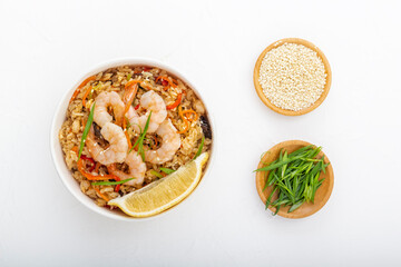 Rice with shrimps, vegetables and lemon in a paper disposable plate on a white table with wooden cups with sesame seeds and green onions. Asian street food. View from above