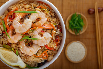 Rice with shrimps, vegetables and lemon in a paper disposable plate on the background of a mat with chopsticks. Asian street food. View from above.