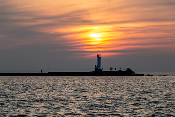 Lighthouse at sunset with people silhouette