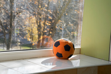 A soft orange football is lying on the window. A ball for classes with young children. The child left the toy on the windowsill