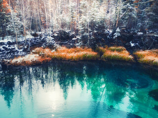 Blue geyser lake in autumn forest after snowfall. Altai mountains, Siberia, Russia. Turquoise lake and snow-covered trees