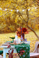 Autumn themed holiday table setting arrangement for a seasonal party, cups, apples, candles, field flowers.