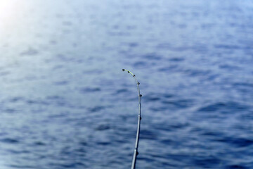 Fishing rod on a background of blue water, selective focus with copy space for text.
