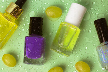 Group of bright nail polishes in bottles and natural green grapes seed cuticle oil in glass bottle with dropper on water drops lettuce background. Colorful nail lacquer. Eco cosmetics beauty products.