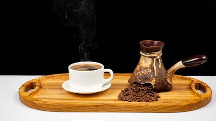 Freshly brewed hot black coffee in a white cup on a wooden board next to a ceramic turkey with coffee beans.