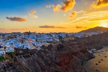 Aerial drone view of famous Oia village with white houses and blue dome churches during sunrise on Santorini island, Aegean sea, Greece.