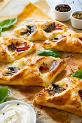 Baked puff pastry with mozzarella, white mushrooms and red bell pepper on baking paper

