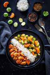Fried chicken nuggets with white rice, brussels sprouts, carrots and tangerines on wooden table
