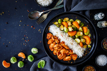 Fried chicken nuggets with white rice, brussels sprouts, carrots and tangerines on wooden table
