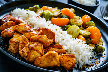 Fried chicken nuggets with white rice, brussels sprouts, carrots and tangerines on wooden table
