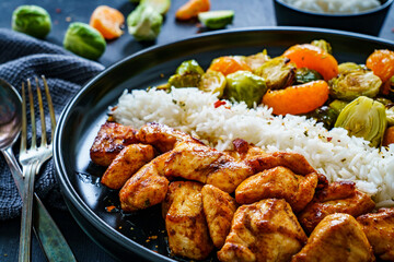 Fototapeta premium Fried chicken nuggets with white rice, brussels sprouts, carrots and tangerines on wooden table 