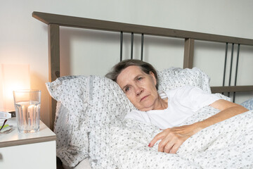 aging senior woman female in bed at home flat, tired sick ill alone retired and resting virus taking care unhappy sad