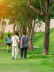 Group of happiness Asian friends talking and walking along the path of park with tall green trees together. The friendship and fun of Asian friends spending their free time outdoors together.