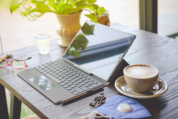 Hot Cappuccino coffee with protective face mask for people work from home by using laptop and stress relief with hot coffee on a table. Concepts of Covid-19 (Coronavirus). Selective focus on coffee.