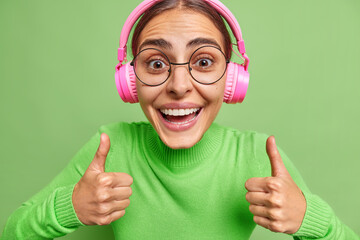 Happy woman enjoys nice audio track does positive gesture with hands keeps thumbs up says I like it...