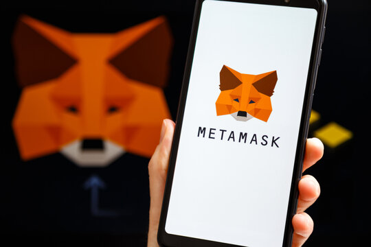 Ukraine, Odessa - October, 9 2021: Hand holding mobile with MetaMask app running at smartphone screen with MetaMask and Binance logo at background. Connecting MetaMask to Binance Smart Chain concept.