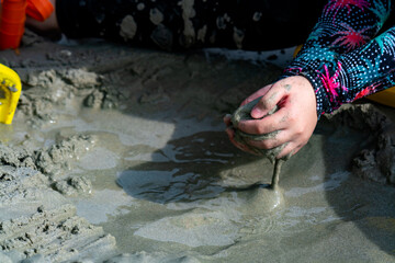 Picture of an Asian girl's hand in a swimsuit. Sitting in a pile of sand by the sea There was wet sand in his hand.