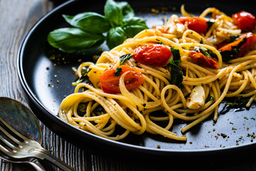 Spaghetti aglio e olio with parmesan, cherry tomatoes and basil on wooden table
