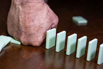 Man hand stopping falling wooden domino effect on white solid background