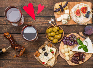 Сheese board with grapes, nuts, fig, dates, olives, wine on rustic wooden background. Top view. Gourmet appetizer for romantic date night. Valentine's Day, love concept.
