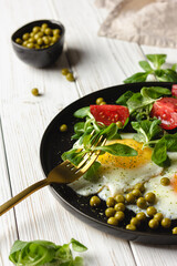 Fried eggs with cherry tomatoes and salad on black plate.