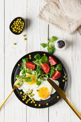 Fried eggs and salad with cherry tomatoes on black plate.