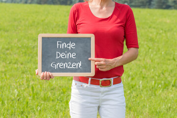 Frau auf einer Wiese mit einer Tafel auf der Finde Deine Grenzen steht
