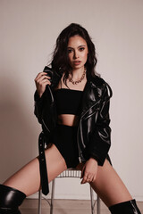 beautiful woman with dark hair in black leather jacket and boots posing in studio